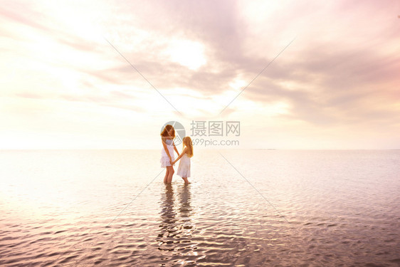 日落时母亲和女儿穿着白裙在海边散步图片