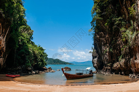 在海滩上KohlantKrbiThlnd附近的KohTalbeng海边悬崖的KohTalbeng海边Krabi和Th木制长尾小艇图片