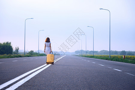 女孩拉着黄色手提箱沿分界线走路图片
