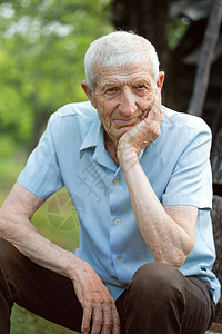 高年男子的肖像坐在花园的里看着摄影机图片