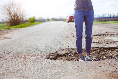 一个女孩站在坏道路的一个洞里图片