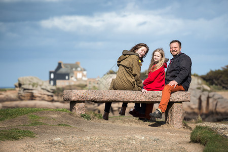 快乐的父亲和两个女儿坐在海边的长凳上图片