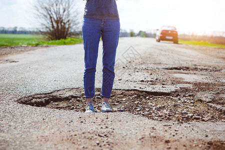 一个女孩站在坏道路的一个洞里图片