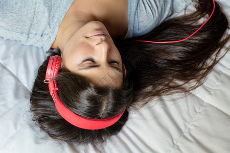 年轻美女躺在床上用耳机听音乐微笑着的女士享受音乐图片