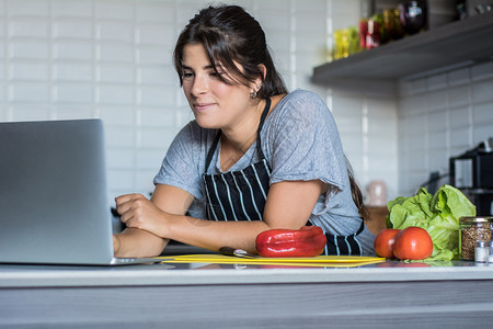 年轻妇女在家中厨房用笔记本电脑食谱做饭和健康品图片