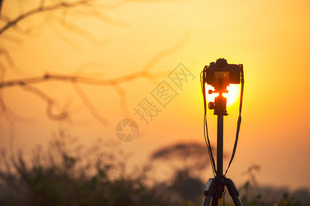 在日落天空的三脚架上安装dslr相机摄影师和概念图片