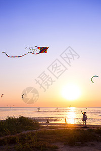 女孩在日落时海面上放风筝背景是美丽的日落海湾图片
