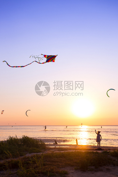 女孩在日落时海面上放风筝背景是美丽的日落海湾图片