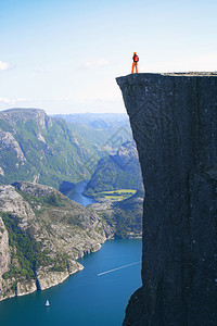 女孩远足者站在前方看着山上在挪威边的著名悬崖上图片