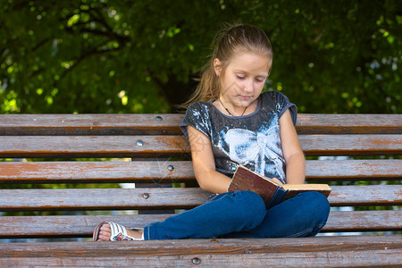 小女孩坐在公园的椅子上看书图片