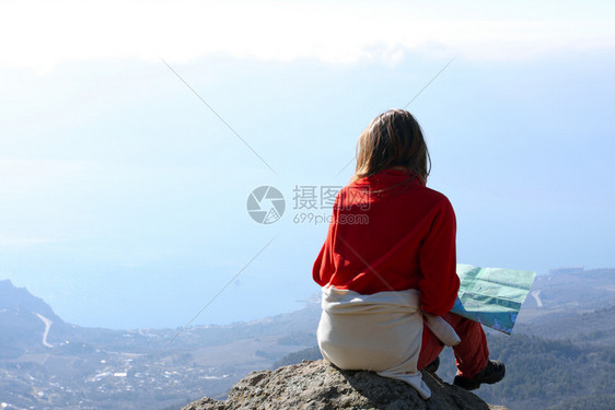 女孩徒步旅行者坐在岩石上看着大海图片