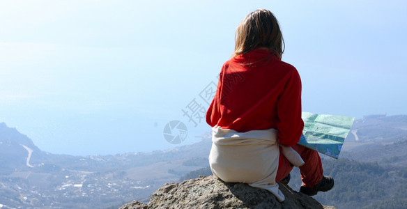 女孩徒步旅行者坐在岩石上看着大海图片