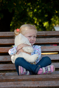 女孩手中抱着泰迪娃娃安静的坐在公园椅子上图片
