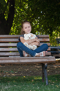 坐在长凳上的女孩与玩具熊在公园图片
