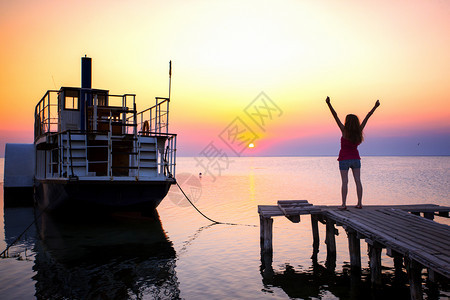 在海船和日落背景的码头上女孩图片