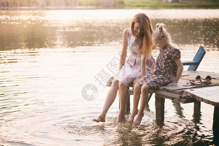 快乐的家庭微笑的母亲和女儿坐在码头上温暖的秋天图片