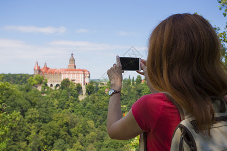 女孩拍照美丽的城堡在山坡上与她的智能手机图片