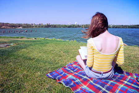 女孩坐在河边的草地上读着一本书图片