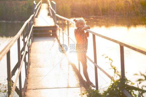 小女孩站在河对岸的桥上看着日落光下的摄像头图片