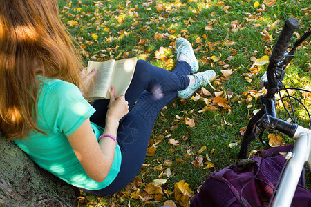 公园里女子带着自行车坐在树下看书图片