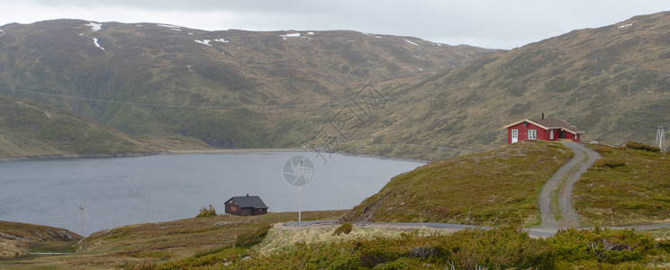 传统挪威木制房屋站在湖边海岸和山丘旁的上图片