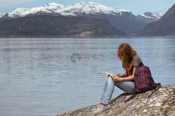 女孩徒步旅行者一本书坐在岩石上山地和湖泊背景上诺威图片