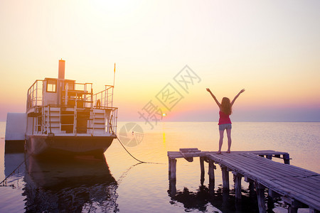 在海船和日落背景的码头上女孩图片
