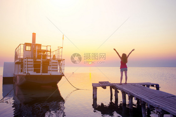 在海船和日落背景的码头上女孩图片