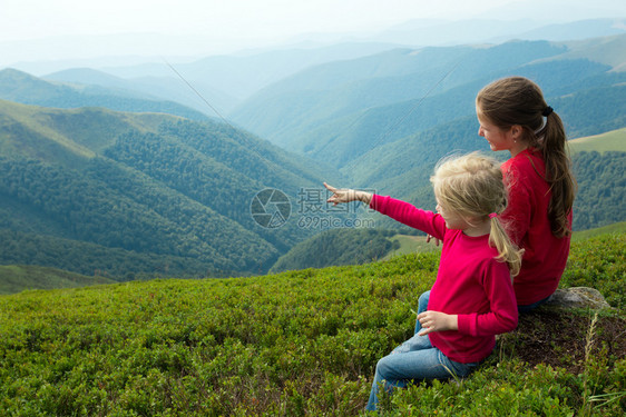 两个女孩坐在草地上看着山图片