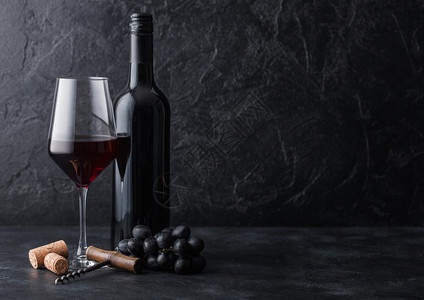 优雅的玻璃和一瓶红葡萄酒装有软木塞和在黑石本底图片
