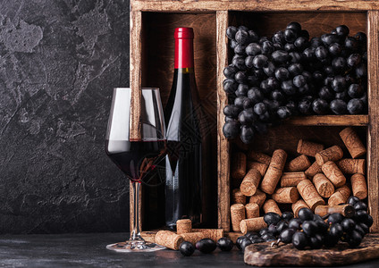 黑石底的旧木箱内装有深葡萄和软木塞的红酒瓶装黑色板上装有软木瓶的优雅葡萄酒杯文本空间图片