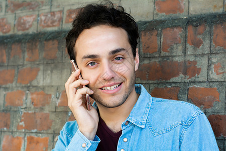 年轻拉丁男子在电话上对着砖墙说的肖像户外图片
