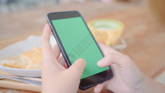 年轻女使用带绿色屏幕的黑手机设备年轻女在咖啡馆坐着时持有智能手机滚动页面铬密钥图片