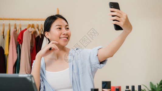 美丽的年轻女使用智能手机自拍在网上流到社交络美容博客在前台平板相机上展示美容化妆品图片