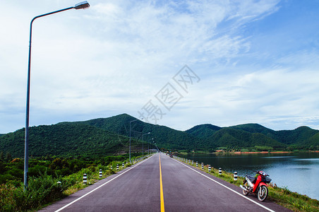 湖边街上老红色摩托车夏季天空和山丘背景图片