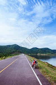 湖边街上老红色摩托车夏季天空和山丘背景图片