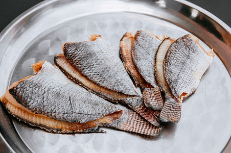 日夫妇用不锈托盘上盐咸罗非鱼干亚裔当地食品保存程序图片