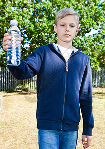 青少年男孩公园里有一瓶水站在草地上背景图片