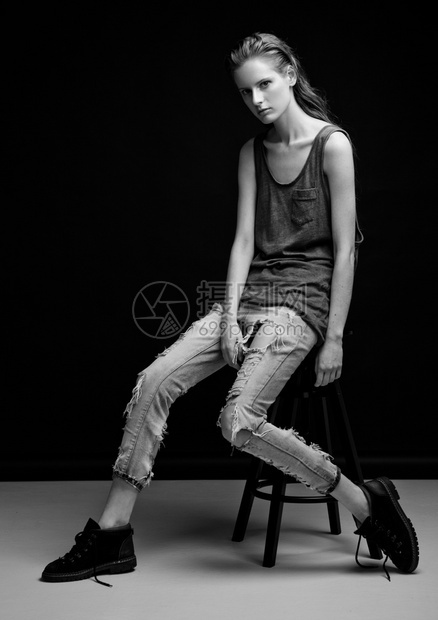 模拟测试年轻漂亮的时装模特身着牛仔裤和衬衫坐在灰色背景的椅子上图片