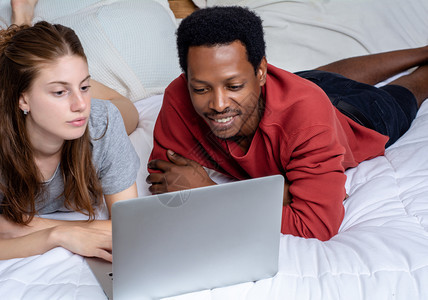 多种族夫妇在家里舒适的床上使用笔记本电脑密室图片