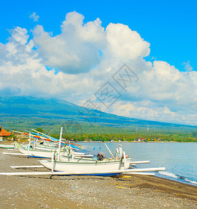 海滩上的阳光天气与传统渔船相伴的海滩上阳光天气在背景巴厘岛因多尼西亚的云层中火山喷发图片