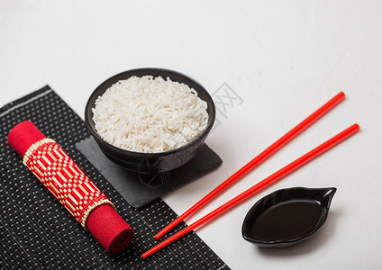 黑碗加煮有机的basmtijsmne大米红筷子和甜豆酱在竹制地垫上红皮巾在黑石上图片