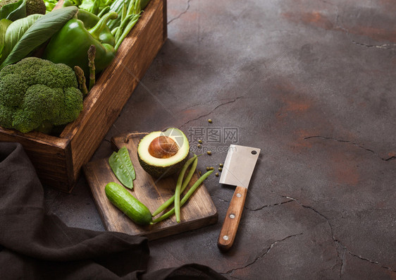 黑石背景的木箱中各种绿色的有机生蔬菜鳄梨卷心菜花椰和黄瓜配有剪断的豆子和用刀砍板图片