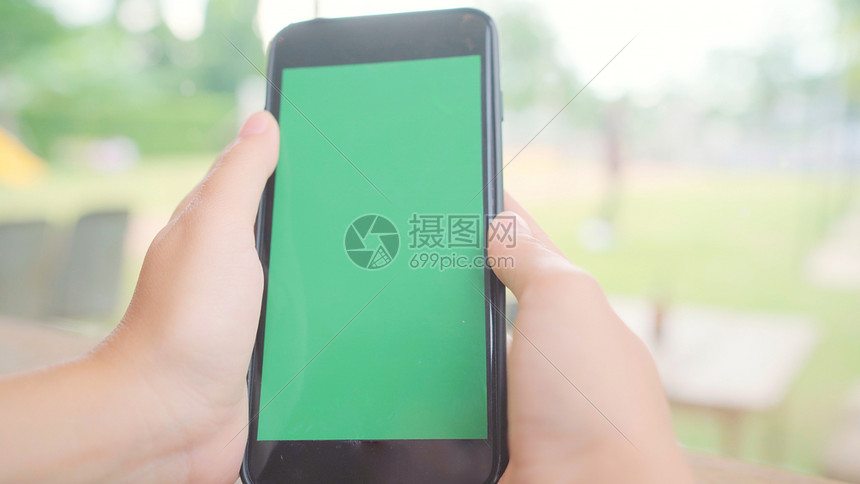年轻女使用带绿色屏幕的黑手机设备年轻女在咖啡馆坐着时持有智能手机滚动页面铬密钥图片