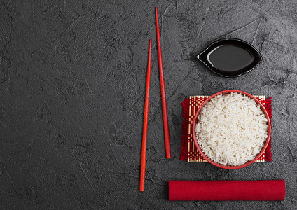 红碗加煮的有机巴斯马提茉米饭红筷子和甜豆酱加竹制地垫红皮巾加黑石本底图片