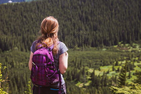 女孩徒步旅行者背着包站在山地和森林中图片