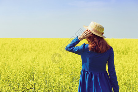 穿着帽子的快乐女孩在乡村的黄色强暴种子田间行走图片