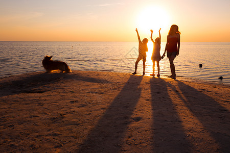 日落时在海滩上行走的母亲女儿和狗图片