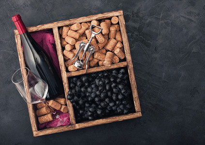 瓶装红酒和空玻璃黑葡萄和深装有软木瓶和箱用黑色的石头背景和红色的布文本空间图片