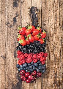 以浅木制桌边的切削板上的新生夏季有机果酱草莓蓝黑和樱桃图片